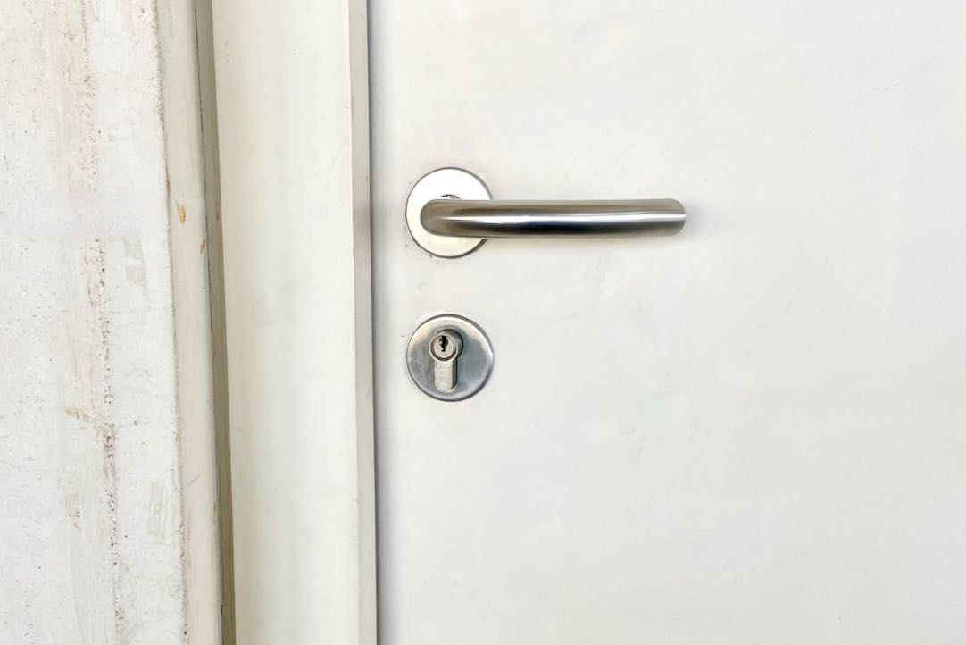 Mecanismo exterior de la puerta de acceso a los aseos comunes de hombres